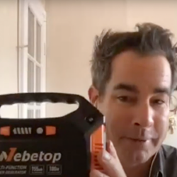 A man holds up a Webetop device, smiling at the camera indoors with a white door behind him—an essential addition to any Go Bag when learning how to prepare for disaster.