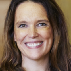 Smiling woman with long brown hair, wearing a dark top, in front of a blurred indoor background—an ideal image for articles on how to engage the private sector effectively.