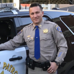 Aristotle Wolfe photo standing in uniform, in front of his patrol car