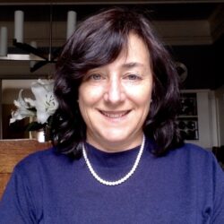 Woman with shoulder-length dark hair, wearing a navy sweater and pearl necklace, smiling indoors while discussing How to Navigate Insurance Before During and After a Disaster with Amy Bach Part 2.