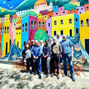 group of people casually dressed and smiling in front of a colorful mural of houses