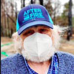close up photo of a white haired man with blue shirt and blue cap with After the Fire printed on it