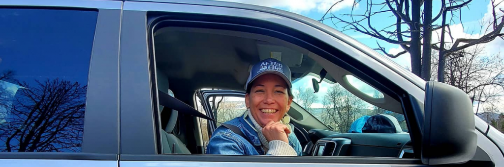 woman in an After the Fire hat looking out the window of a truck and smiling