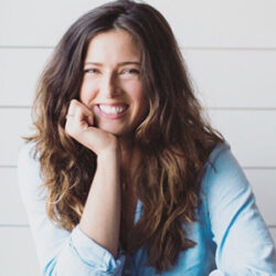 Smiling woman with long brown hair wearing a light blue shirt, resting her chin on her hand. Jacqui Jorgeson contemplates the details of a rebuild permit with confidence and ease.