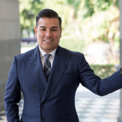Man in a blue suit standing outdoors, smiling confidently, with trees and greenery in the background—perfectly capturing the peace of mind that comes with having reliable homeowner's insurance.