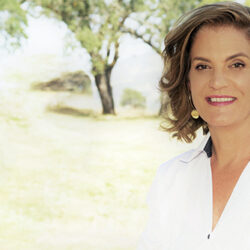 Woman with shoulder-length brown hair in a white shirt smiling outdoors with trees in the background, radiating hope after the fire.