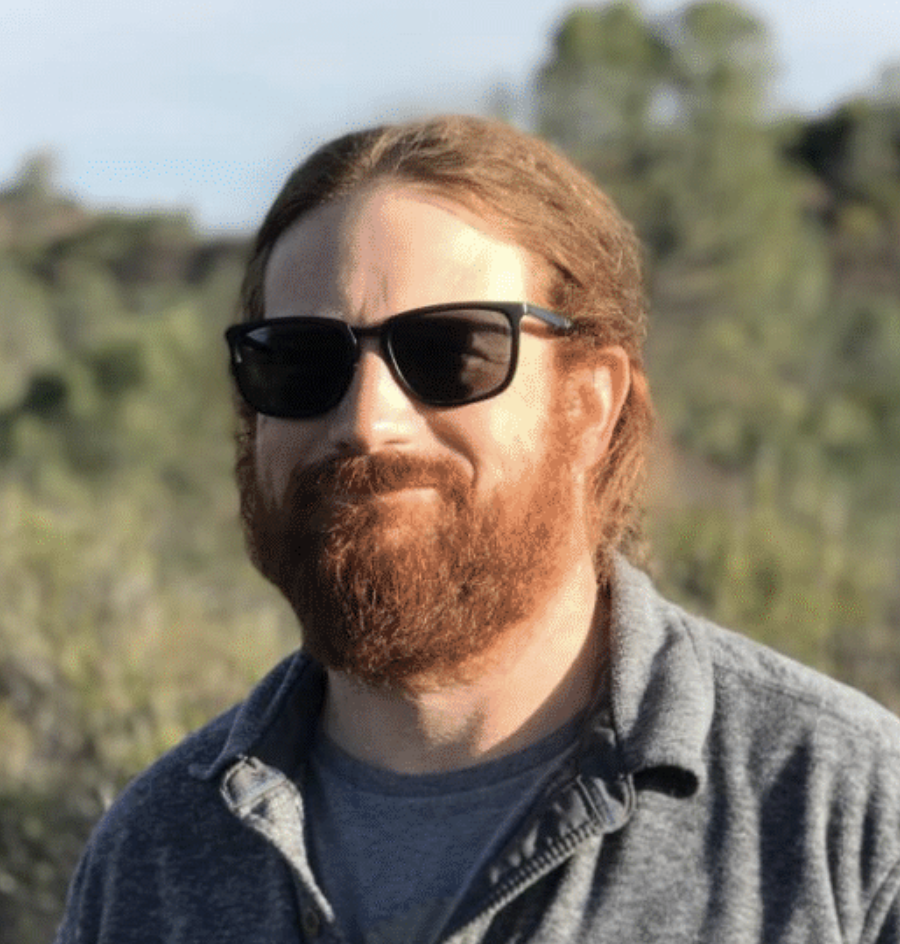 man with red hair and beard outdoors smiles for the camera