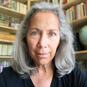 woman with shoulder length gray hair and black shirt looking at the camera with bookshelves behind