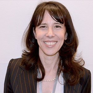 Smiling woman with long dark hair, a member of the Board of Directors, wears a pinstripe blazer, white top, and pearl necklace.