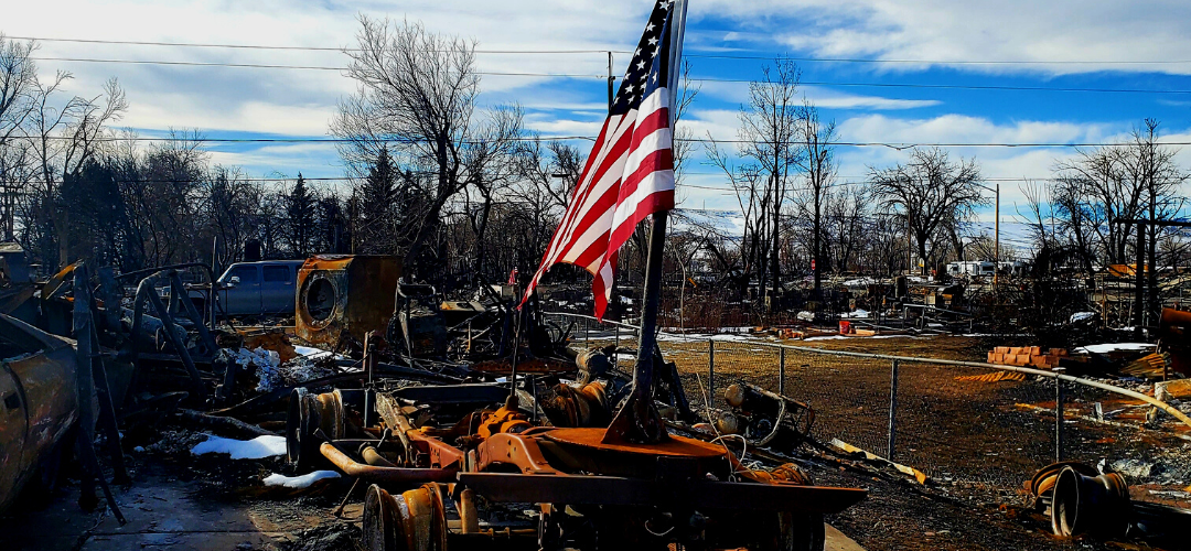 American Flag on a pole set amidst burned and rusted debris from a wildfire
