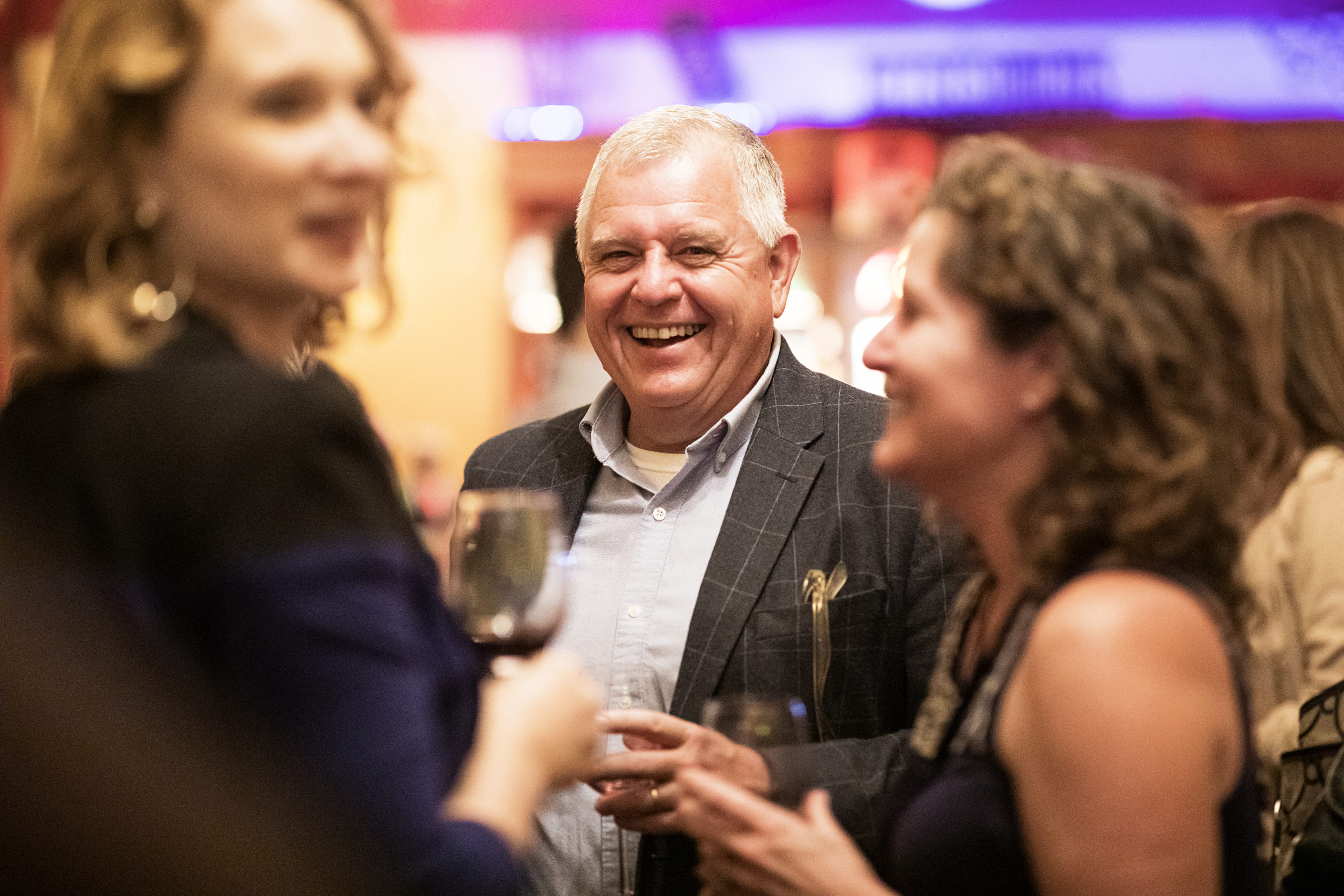 man smiling as he listens to two women at a reception
