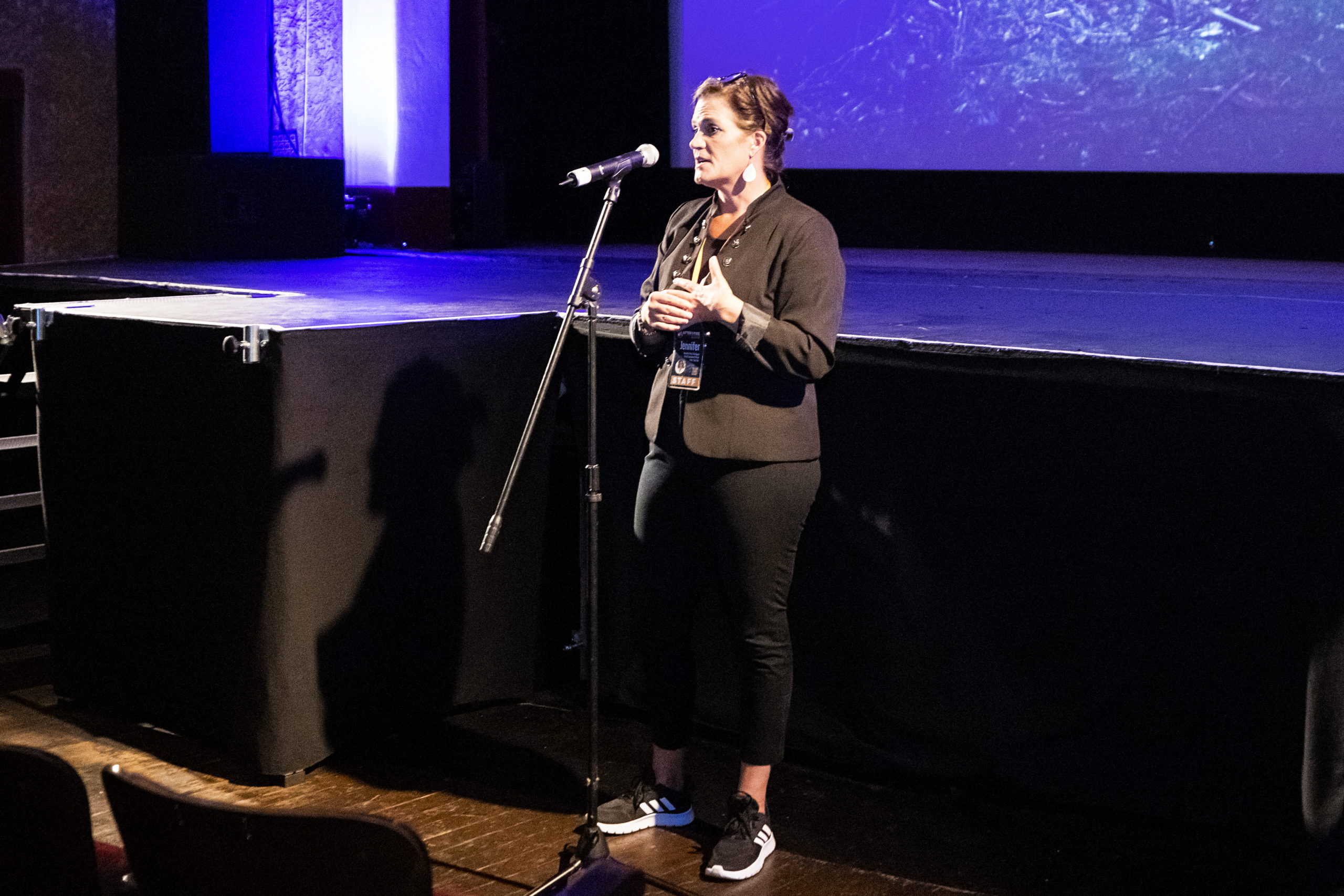 Woman speaking in a microphone in front of a darkened movie theater