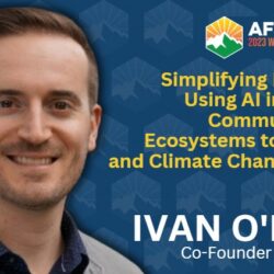 Ivan ONeill smiles in front of a summit banner about AI, wildfire resilience, and climate change adaptation at the Wildfire Leadership Summit.
