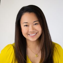 Reina Pomeroy, with long dark hair, wears a yellow top and gold necklace, smiling at the camera against a white background.