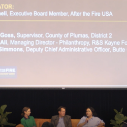 Four panelists speak onstage beneath a large screen displaying their names and titles at an event.