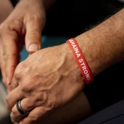 Close-up of hands; one wrist wears a red bracelet that reads LAHAINA STRONG in white letters.