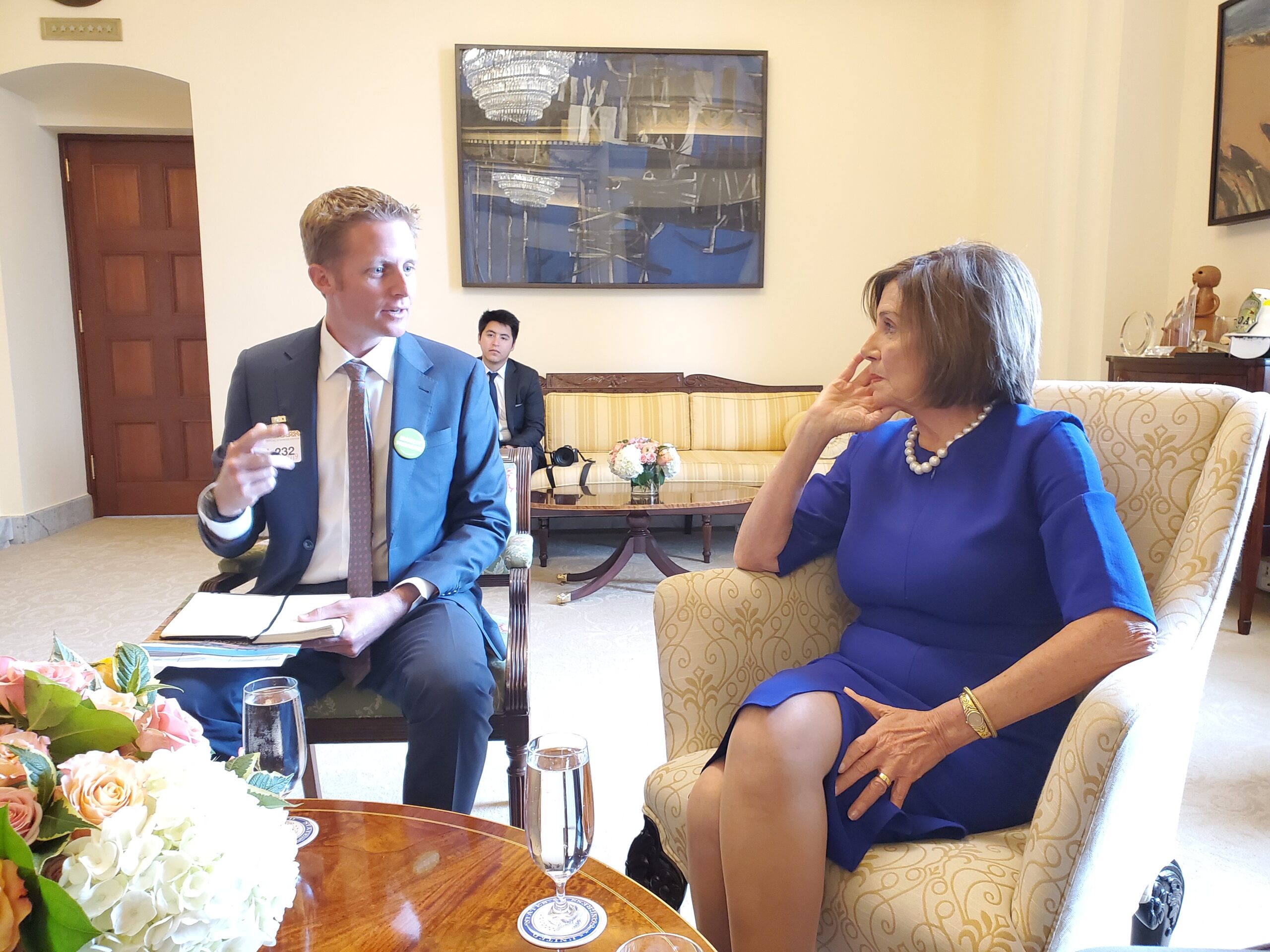 A man and his partner sit and talk in an elegant room, with flowers and water glasses on the table in front of them, reflecting quietly after the fire.