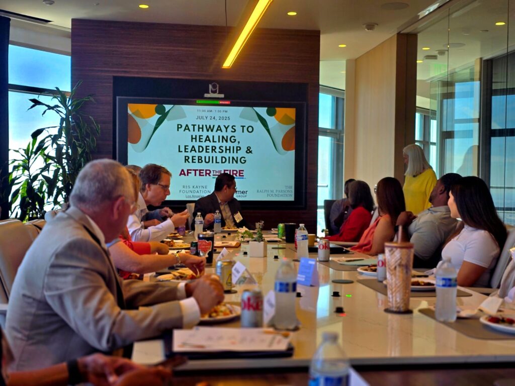 People in a conference room watch a screen displaying “Pathways to Healing, Leadership & Rebuilding After Fire.