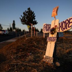 Wooden angel sign by roadside reads Faith Hope Paradise at sunset, with cars and trees in the background.