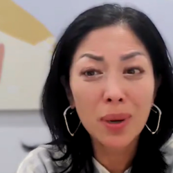 A woman with dark hair and hoop earrings speaks emotionally during a video call.