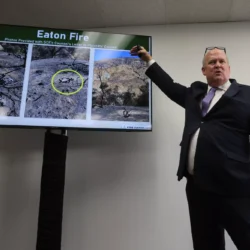 A man in a suit points to wildfire damage photos labeled Eaton Fire on a screen during a presentation.