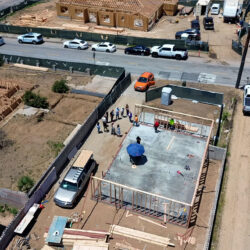 Aerial view of a house under construction with workers gathered on a concrete foundation.