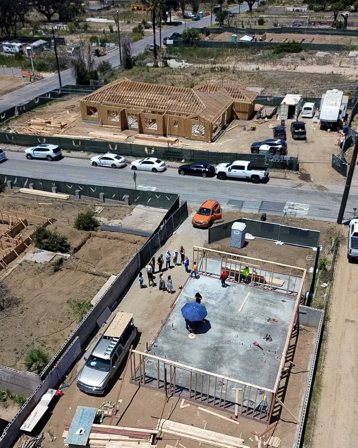 Aerial view of a house under construction, people are gathered on a concrete foundation nearby, discussing resiliency programs that support strong and sustainable communities.