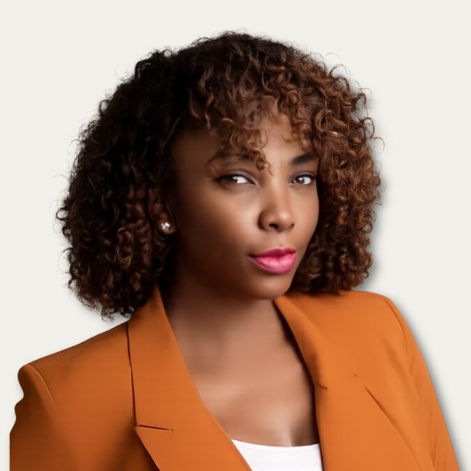 Woman with curly brown hair in an orange blazer, looking confidently at the camera, white background.