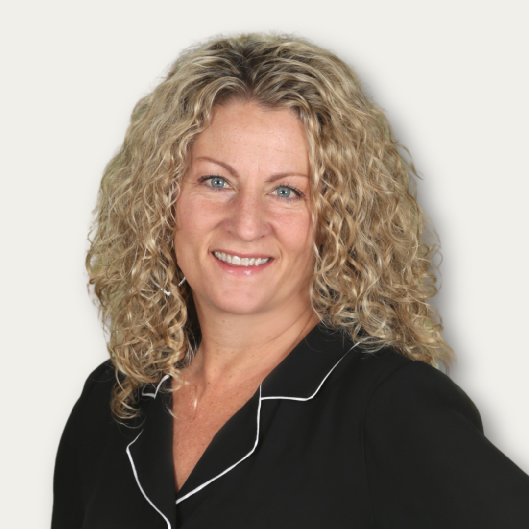 Smiling woman with curly blonde hair wearing a black top, posing in front of a plain light background.