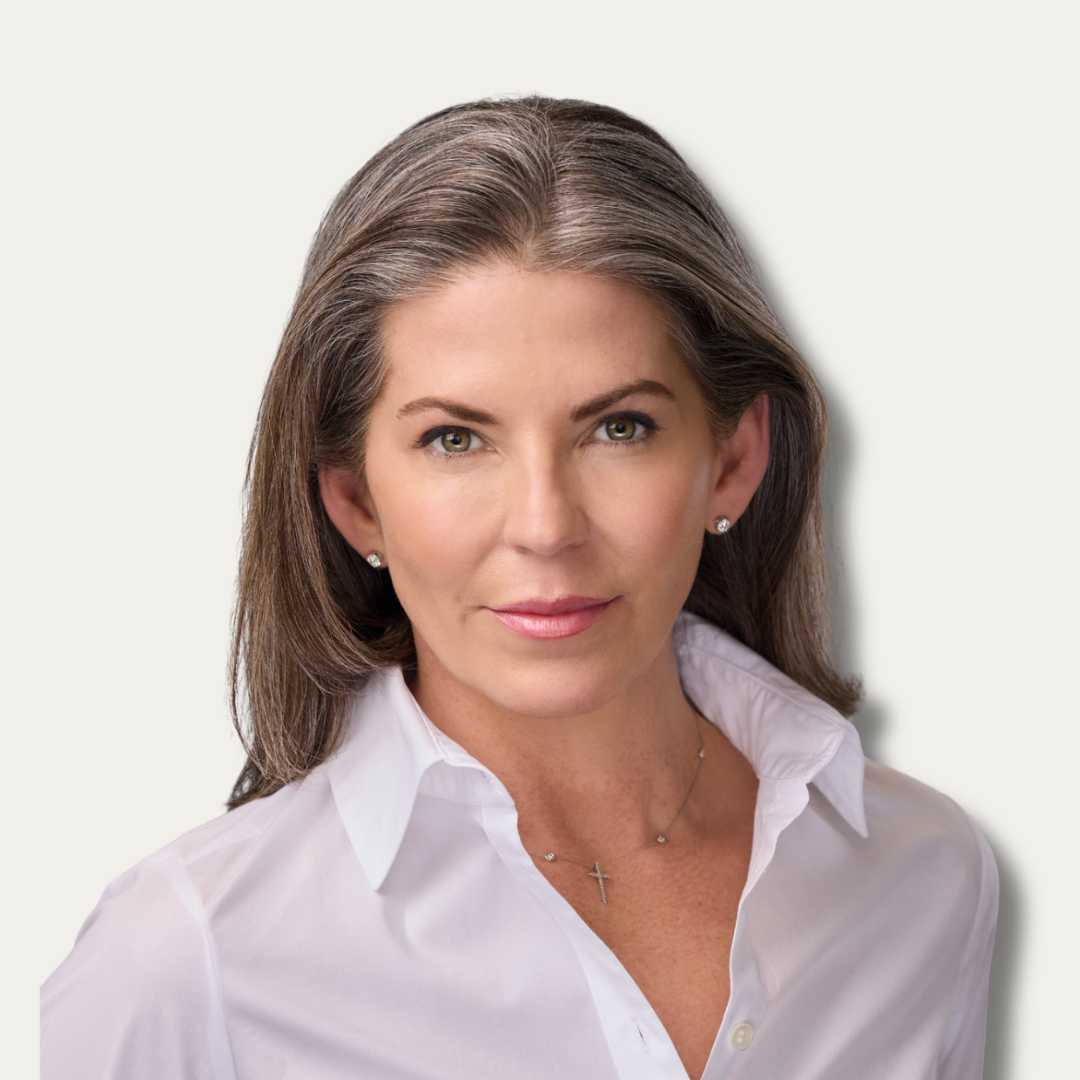Woman with long gray hair wearing a white shirt, necklace, and stud earrings, facing the camera.