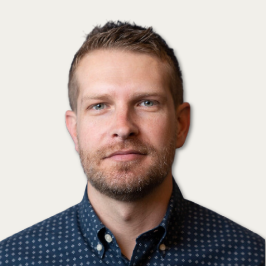 Man with short hair and beard wearing a navy patterned shirt, looking at the camera with a neutral expression.