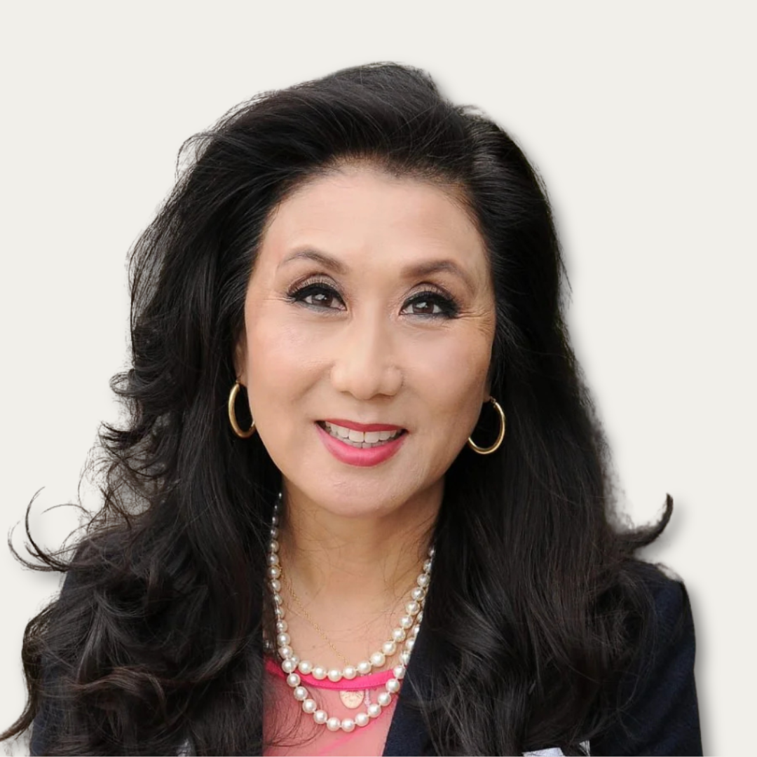 Smiling woman with long black hair, gold hoop earrings, and layered pearl necklaces against a light background.