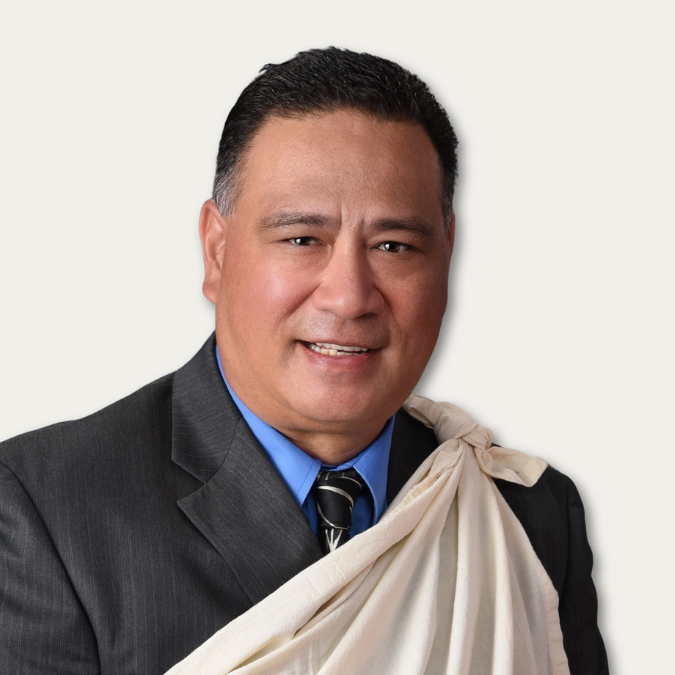 Man in a suit and tie with a cream-colored cloth draped over his shoulder, smiling at the camera.