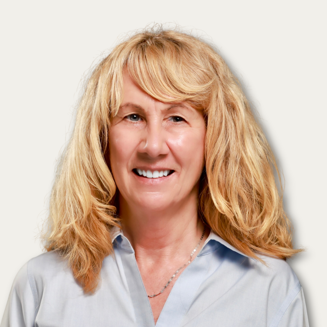 Smiling woman with blonde, wavy hair wearing a light blue collared shirt, against a plain background.