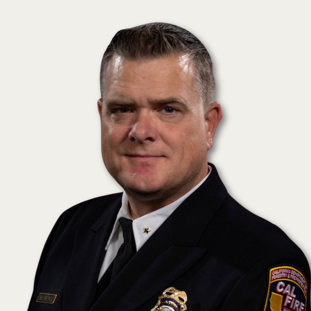 Man in a CAL FIRE uniform, wearing a badge, posing for a professional portrait against a plain background.