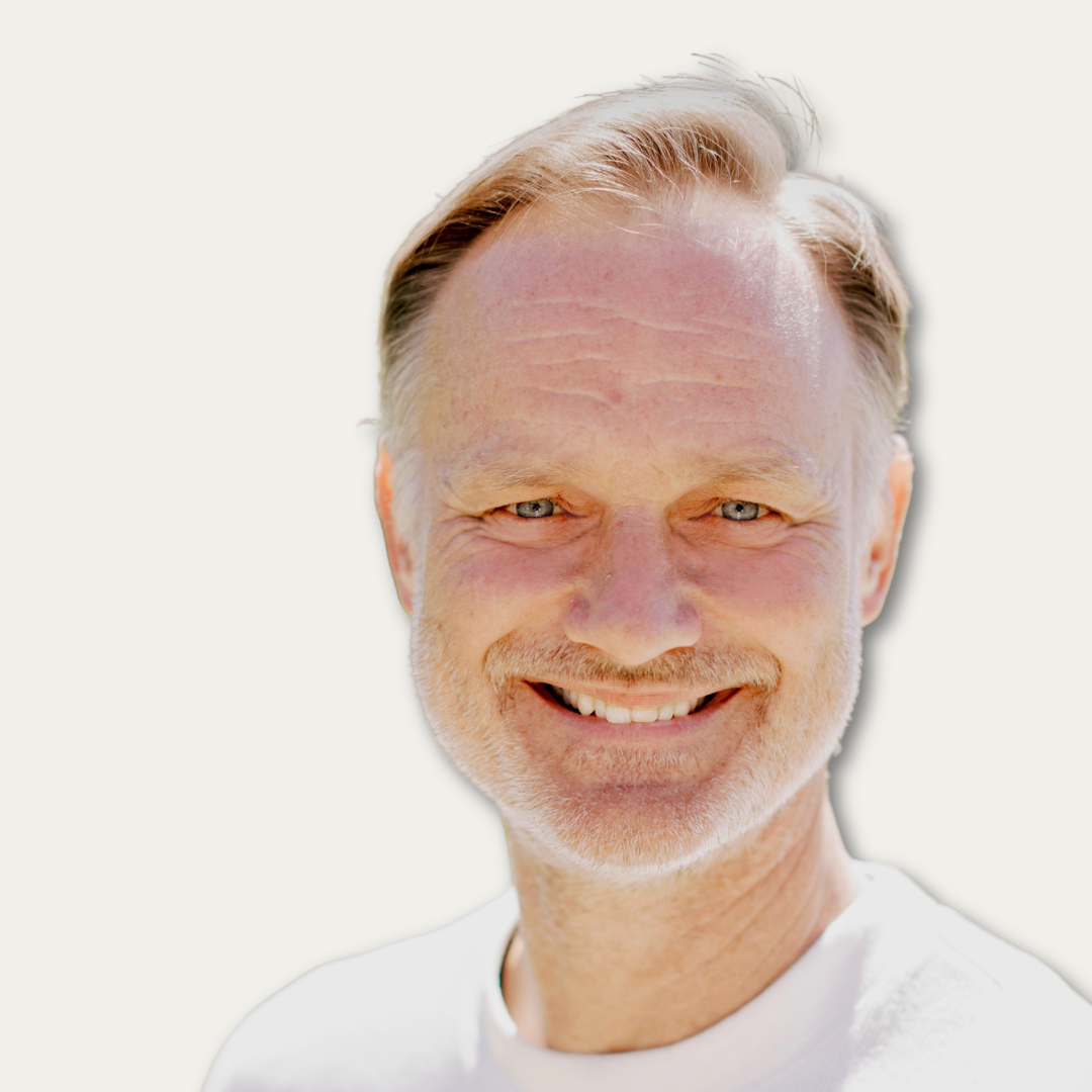 Middle-aged man with light hair and beard smiling, wearing a white shirt, on a light background.