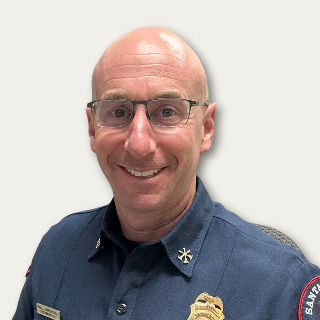 Smiling man in a navy uniform with glasses, a badge, and fire department insignia on his shoulders.