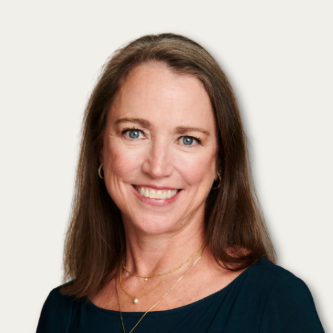 Smiling woman with straight brown hair in a navy top, wearing gold earrings and layered necklaces.