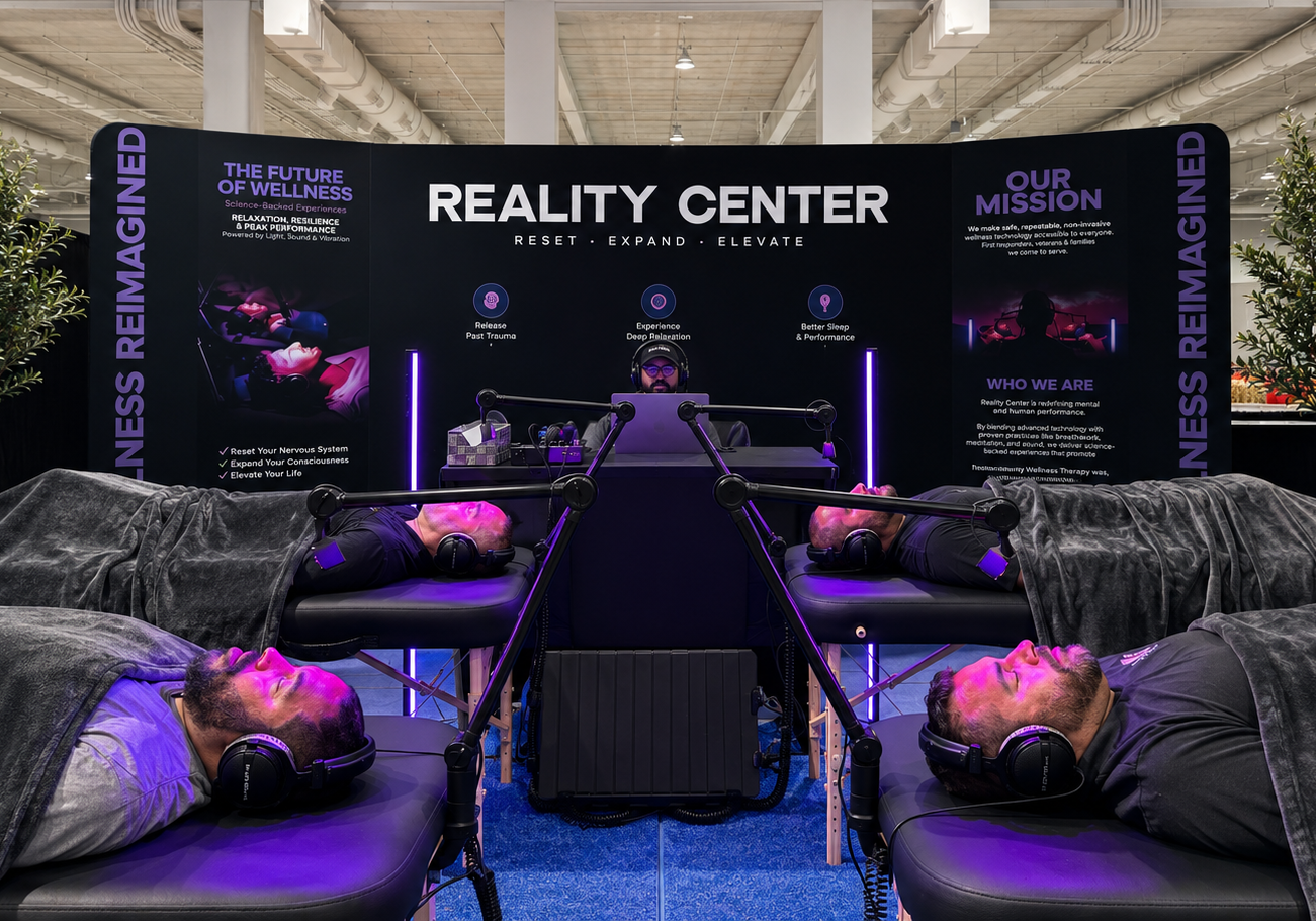 Four people relax on reclining chairs with headsets in a modern wellness center with dark, calming decor.