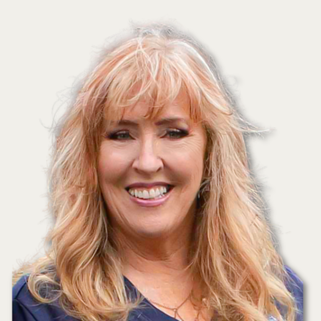 Smiling woman with long blonde hair wearing a blue top, photographed against a plain light background.