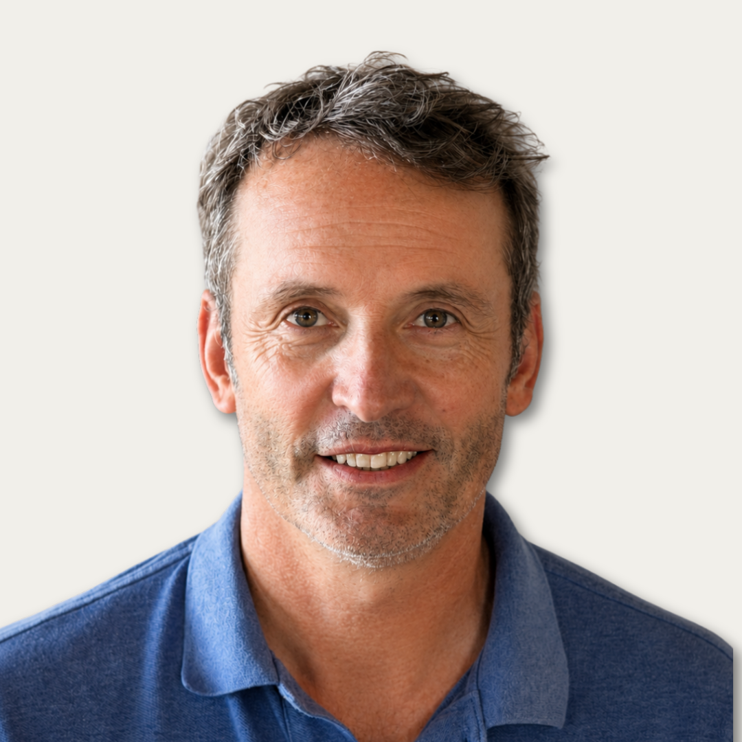 Smiling middle-aged man with short brown hair, wearing a blue polo shirt, in front of a plain background.