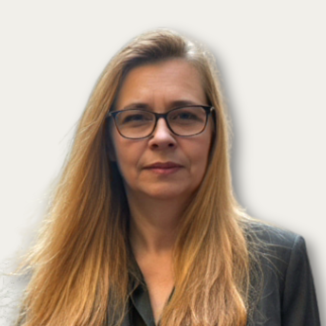 Woman with long blonde hair and glasses wearing a dark blazer, facing forward against a light background.